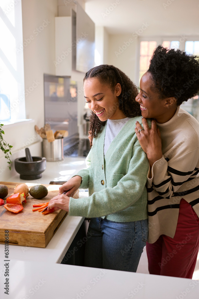 Mother With Teenage Daughter Helping To Prepare Meal At Home In Kitchen Together