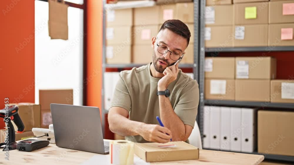 Young hispanic man ecommerce business worker talking on smartphone writing address on package at office Young hispanic man ecommerce business worker talking on smartphone writing address on package at office