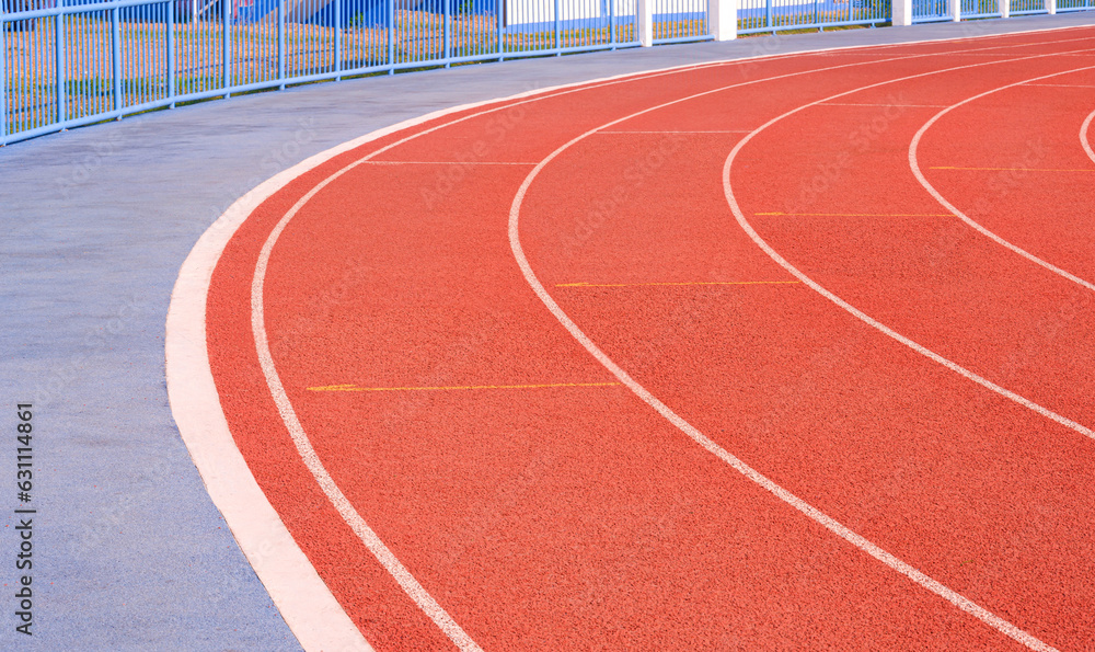 Empty red curve synthetic running tracks with concrete pavement and fence in athletic outdoors stadium