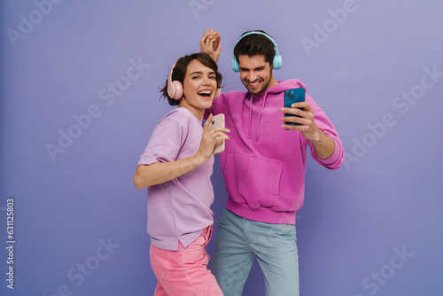 Young couple dancing while listening music with headphones and mobile phones isolated over purple background