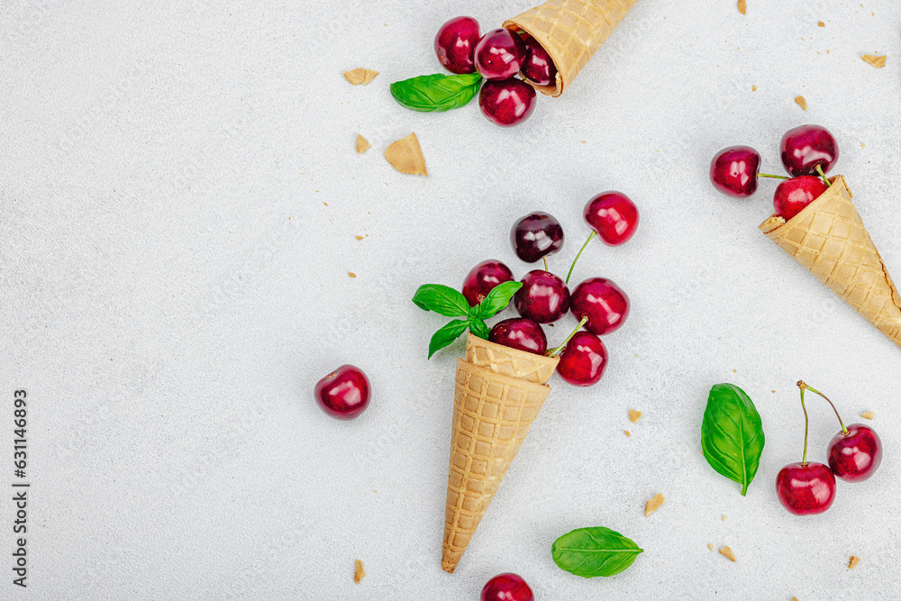 Ripe sweet cherries in waffle cones on light stone concrete background. Flat lay, vintage napkin Ripe sweet cherries in waffle cones on light stone concrete background. Flat lay, vintage napkin