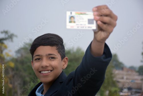 Indian school boy wearing dark blue school uniform, with smiling face shows her blurred aadhar card in her hand. blurry background