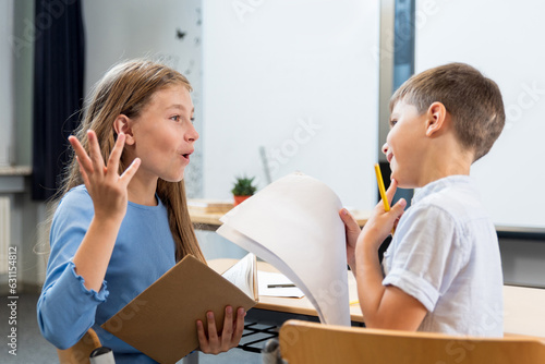 Lively conversation of children in the classroom. A schoolgirl explains to her desk mate how letters are written. The boy is interested and thoughtful. Creative communication of children as teacher.