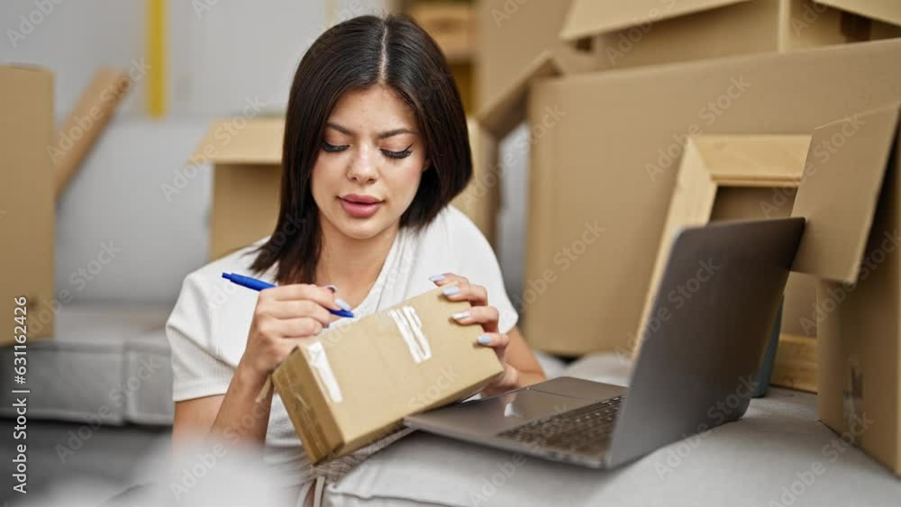 Young caucasian woman using laptop writing on package at new home Young caucasian woman using laptop writing on package at new home