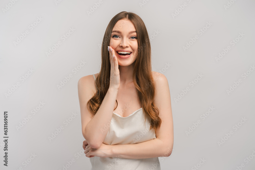 Smiling woman in dress feeling happy and surprised holding hand on face, looking at camera Smiling woman in dress feeling happy and surprised holding hand on face, looking at camera