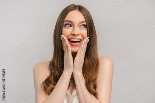 Smiling woman in dress feeling happy and surprised holding hand on face, looking away