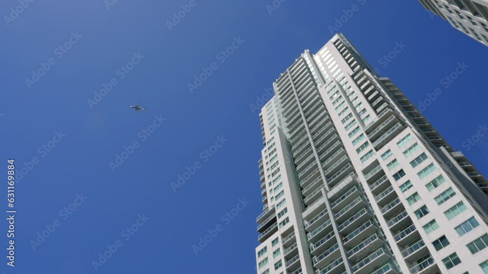 Spectacular low angle view of high contemporary skyscraper connecting with clear blue sky while plane gracefully flying overhead. Concept of human achievements and modern world Spectacular low angle view of high contemporary skyscraper connecting with clear blue sky while plane gracefully flying overhead. Concept of human achievements and modern world