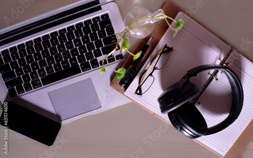 Top view of office Workplace with open laptop, a blank open note book, a smart phone ,a pen, a specs and a head phone on a wooden desk