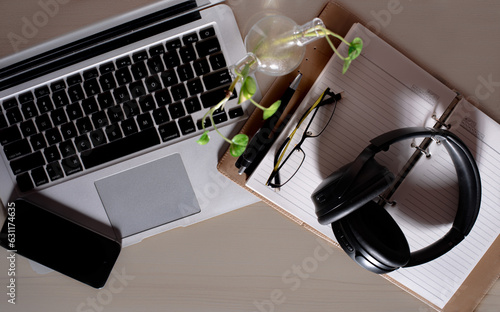 Top view of office Workplace with open laptop, a blank open note book, a smart phone ,a pen, a specs and a head phone on a wooden desk
