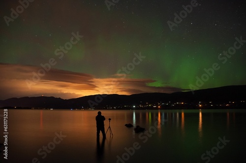 Silhouette of a photographer with a camera on a tripod under the Northern Lights on Okanagan Lake