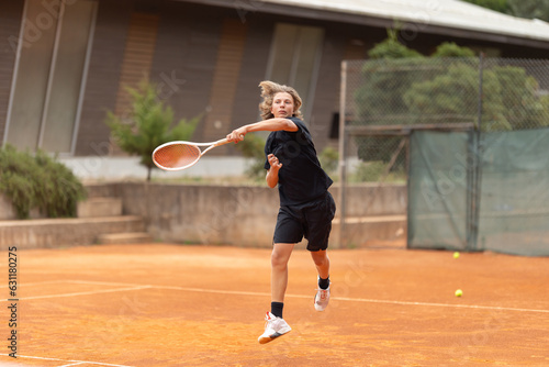 A boy teenager in black t-shirt playing tennis on the court - frame in motion - hitting back the ball © KONSTANTIN SHISHKIN