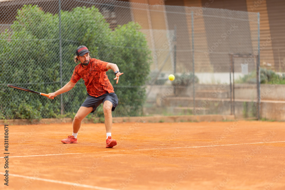 An adult man in red t-shirt playing tennis on the court