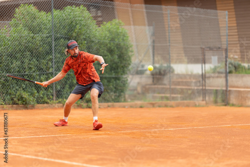 An adult man in red t-shirt playing tennis on the court © KONSTANTIN SHISHKIN