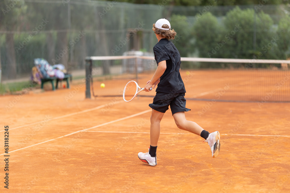 A boy teenager in a black t-shirt running on the tennis court to hit back the ball