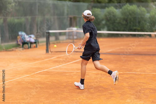 A boy teenager in a black t-shirt running on the tennis court to hit back the ball © KONSTANTIN SHISHKIN