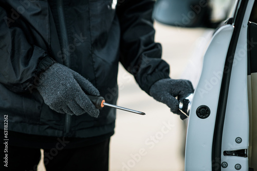 Man dressed in black holding screwdriver to break lock and steal a vehicle on the road  Social destruction  Insurance  Car thief concept.