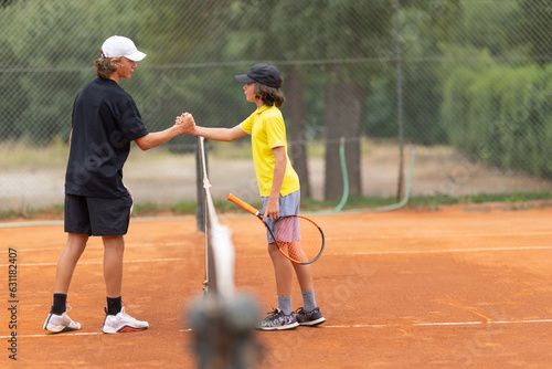 Two boys shake hands above the net on the tennis court © KONSTANTIN SHISHKIN