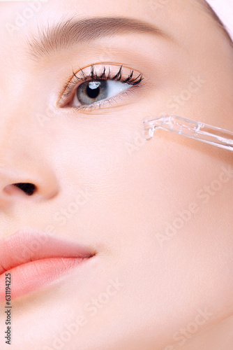 Beautiful young white woman applying serum on her face closeup
