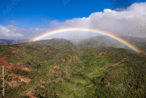 Aerial view of a rainbow over green mountains in Waimea Canyon State Park in Kauai County, Hawaii