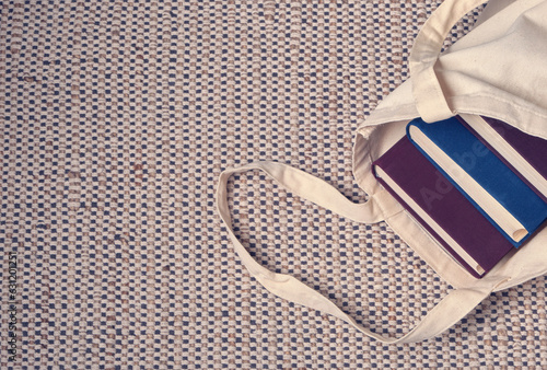 Clever weighty books in textured blue and lilac fabric covers lie in an open linen bag on a natural jute and cotton carpet. Unpacking book purchases, lifestyle, habit of reading