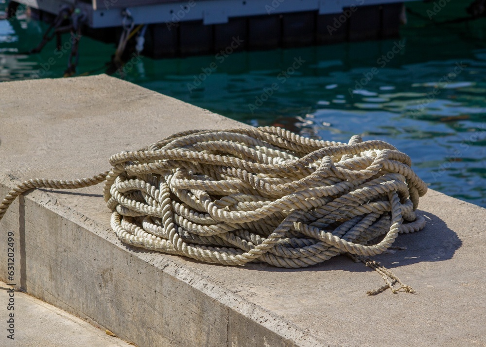 Fototapeta premium Coiled rope lies on a block near a tranquil lake under the sun