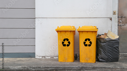 Yellow recycle bins and black waste plastic bag on dark ground and white wall in background  concept of recycle waste                               