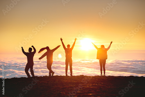 Group of happy tourists are having fun and dance at sunrise on mountain top over clouds