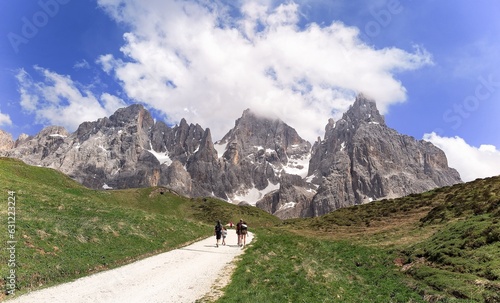 Tourists hiking on a track towards Cimon della Pala amid rugged peaks of Pale di San Martino mountain range in Dolomites on a sunny summer day, in Passo Rolle, Trentino Alto Adige, South Tyrol, Italy