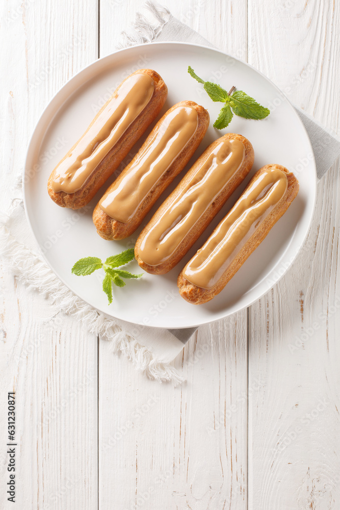 Fresh classic eclairs with cream filling and covered with caramel sauce close-up in a plate on the table. Vertical top view from above Fresh classic eclairs with cream filling and covered with caramel sauce close-up in a plate on the table. Vertical top view from above