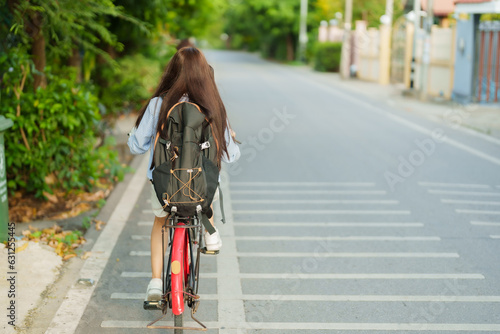 Fototapeta Naklejka Na Ścianę i Meble -  The back of a long-haired Asian woman riding a bicycle on a road in a rural community to travel and see the way of life of rural communities. To relax after tiring work on a long weekend