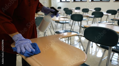Obraz na plátně Closeup of woman teacher hands with spray bottle, gloves, rag, wiping, cleaning and disinfecting school desks