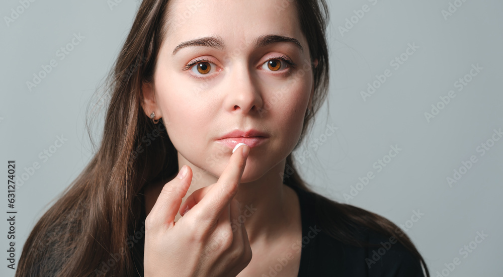 Virus herpes on lips close-up. Beautiful woman holds on finger a cream drop in front of painful lips. Portrait of young beautiful girl European appearance with infection injury. Dermatology sickness Virus herpes on lips close-up. Beautiful woman holds on finger a cream drop in front of painful lips. Portrait of young beautiful girl European appearance with infection injury. Dermatology sickness