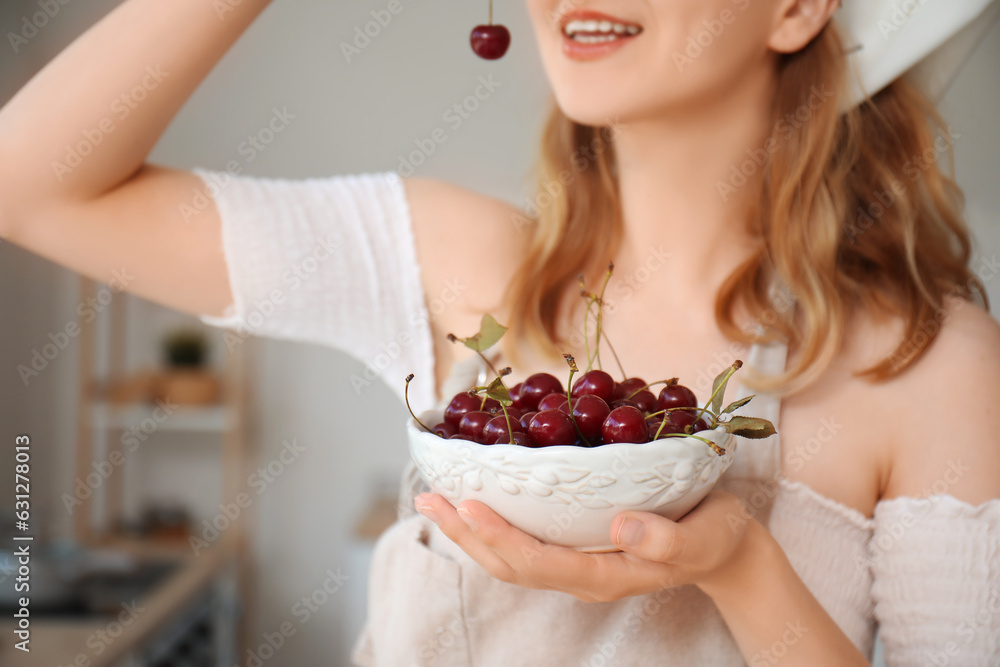 Beautiful happy young woman eating ripe cherries in kitchen Beautiful happy young woman eating ripe cherries in kitchen