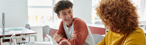 Принти на полотні Smiling teen schoolboy talking to classmate near devices during lesson in classr