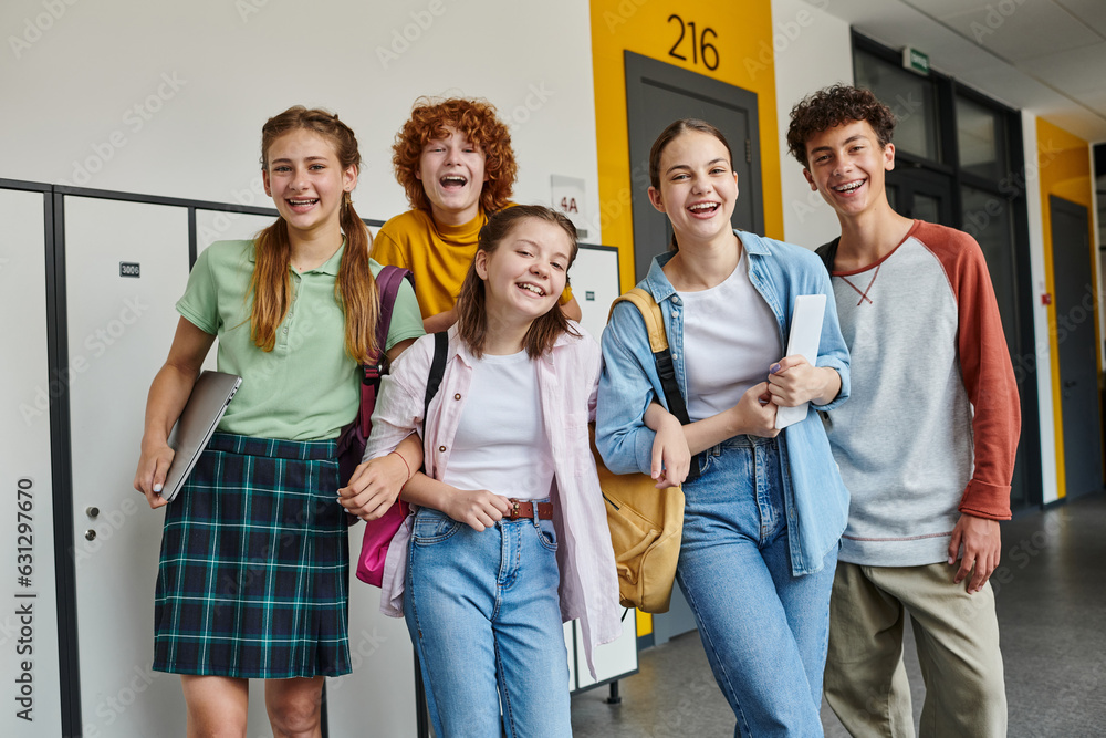 Obraz premium teenage schoolkids looking at camera and standing in school hallway, teen classmates with devices