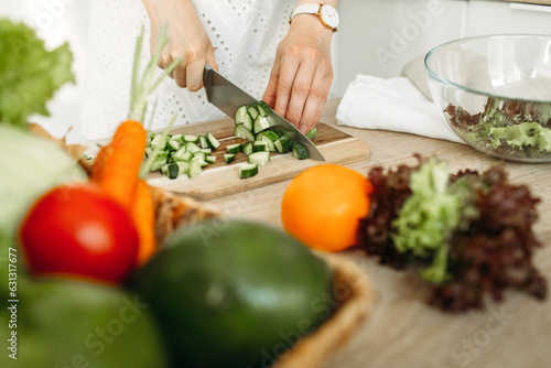 A woman cuts a cucumber with a knife on the background of vegetables lying on the table.