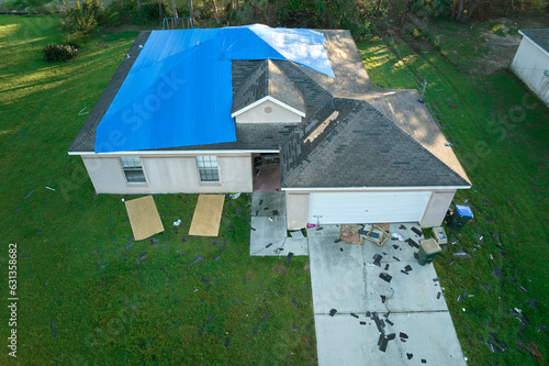Hurricane Ian damaged house rooftop covered with protective plastic tarp against rain water leaking until replacement of asphalt shingles. Aftermath of natural disaster