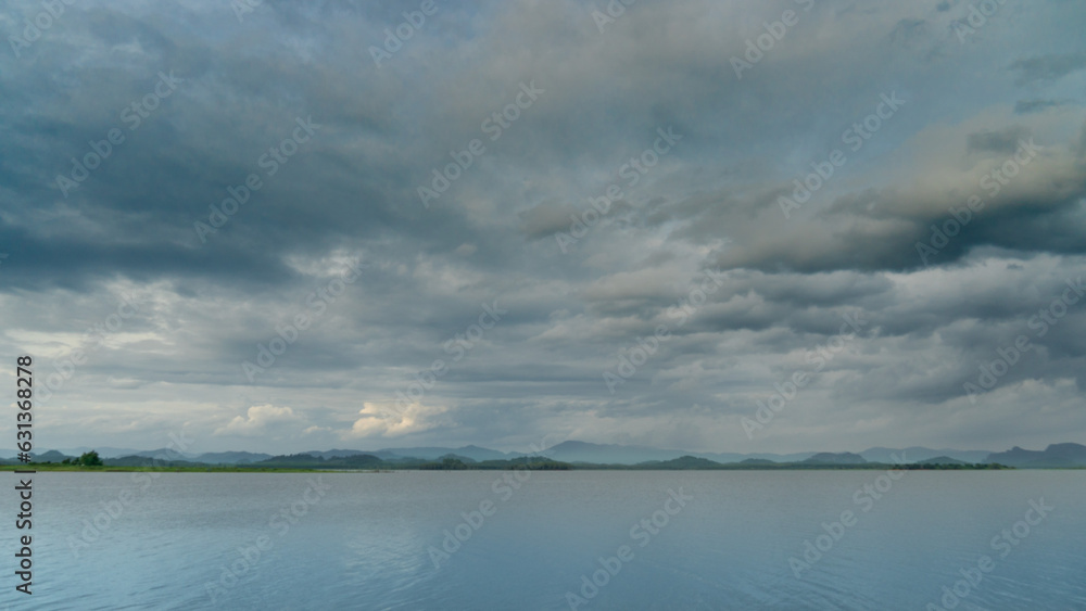 Landscape view of large river or reservoir. Location name of Pra Sae Reservoir. Background of distant mountains shrouded in mist under the dim sky.