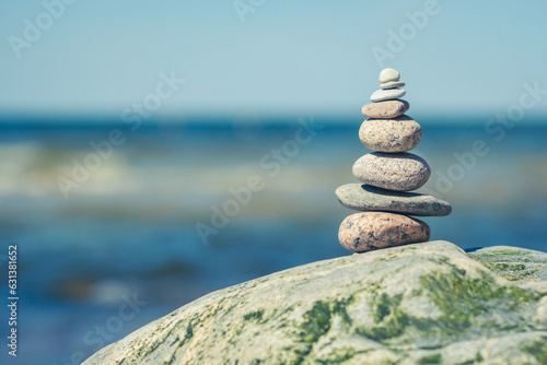 Balancing stones on a big rock with sea grass on the beach, with blue water waves on background, Baltic Sea, Olando Kepure, Lithuania photo