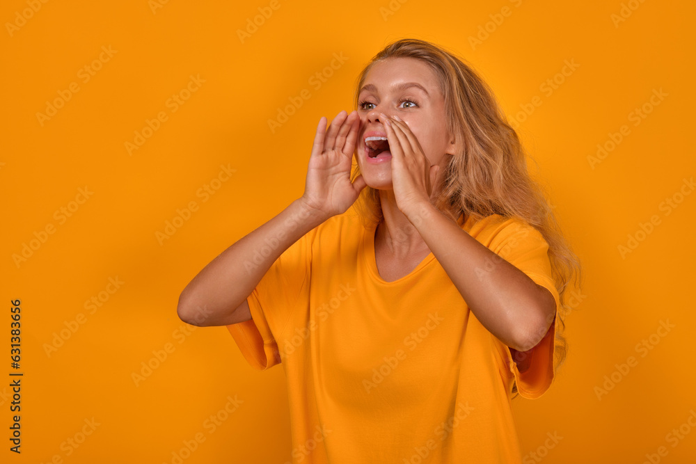 Young noisy energetic Caucasian woman promoter puts hands to mouth instead of megaphone and shouts announcing opening of new shopping mall stands on yellow studio background. Advertising, marketing Young noisy energetic Caucasian woman promoter puts hands to mouth instead of megaphone and shouts announcing opening of new shopping mall stands on yellow studio background. Advertising, marketing