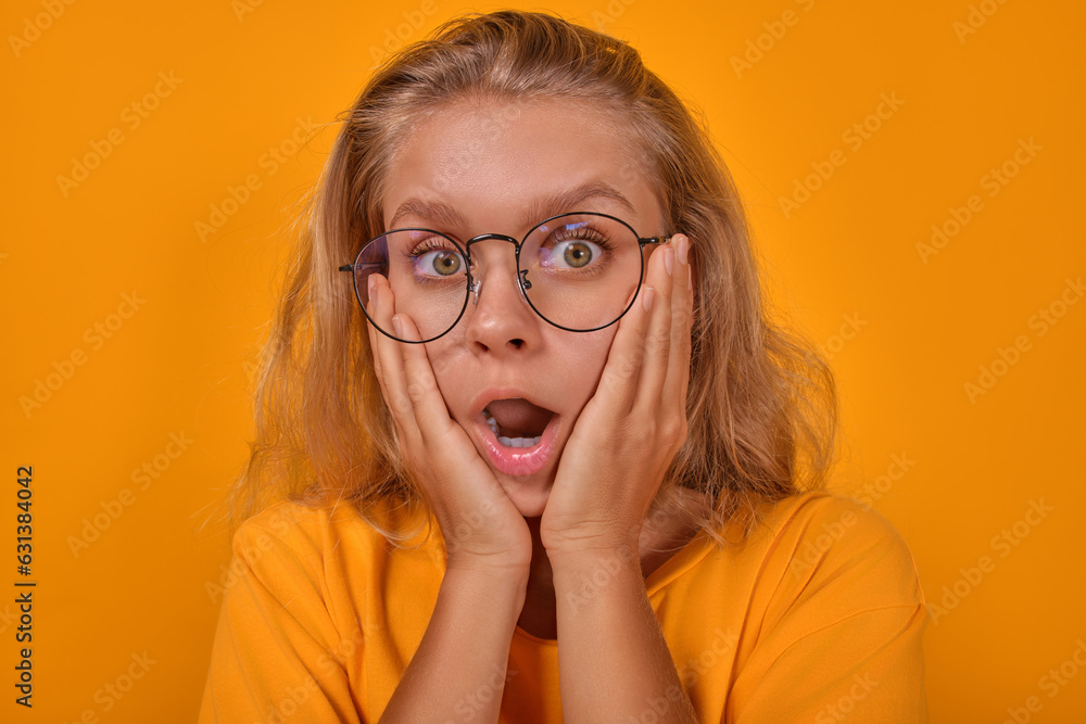 Young shocked attractive Caucasian woman student with open mouth looks at screen because of amazing news from university or lot of extracurricular work stands in yellow studio. High school pupil Young shocked attractive Caucasian woman student with open mouth looks at screen because of amazing news from university or lot of extracurricular work stands in yellow studio. High school pupil