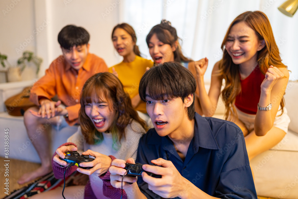 Group of Young Asian man and woman playing video games together in living room at home. Happy people friends enjoy and fun indoor activity lifestyle spending time together on holiday vacation.