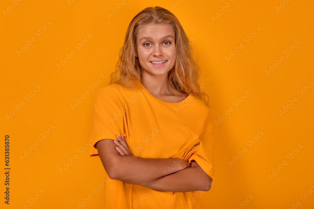 Obraz premium Young confident beautiful Caucasian woman blonde stands with arms crossed and looks at camera with smile demonstrating positive emotions and self-confidence posing on isolated yellow background.