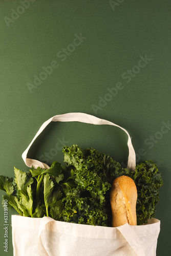 White canvas bag with baguette and green salad vegetables and copy space on green background