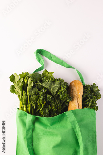 Green canvas bag with baguette and green salad vegetables and copy space on white background