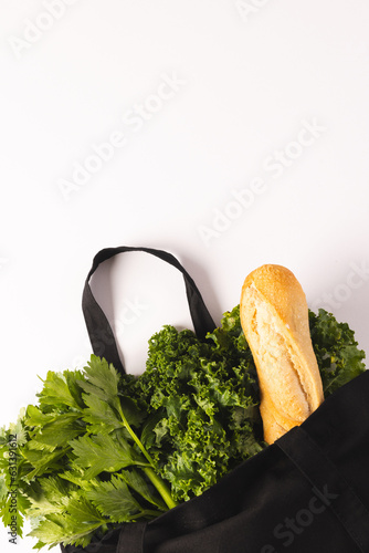 Black canvas bag with baguette and green salad vegetables and copy space on white background
