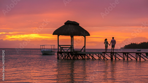 Man and Woman with hands together watching sunset on a wooden pier in the ocean on a tropical beach in Mauritius, a couple on a honeymoon vacation in Mauritius