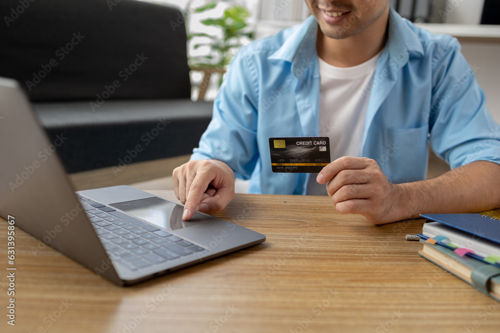 Asian man holding a credit card, he is filling in credit to pay for goods and services on the internet, using credit card to pay for services. Credit card spending concept. Asian man holding a credit card, he is filling in credit to pay for goods and services on the internet, using credit card to pay for services. Credit card spending concept.