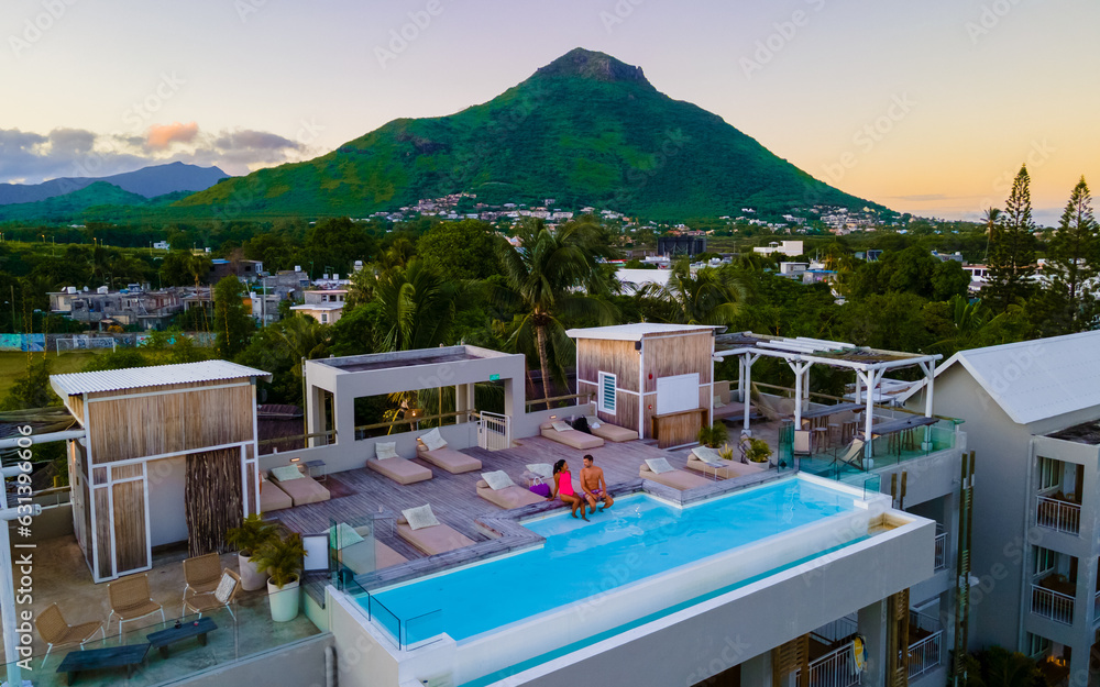 Men and Woman watching sunrise by a swimming pool, a couple on a honeymoon vacation in Mauritius with on the background the Tamarin mountain