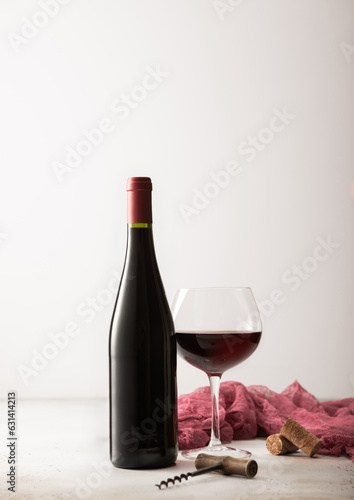 Glass and bottle of red wine with red towel and corkscrew on light background.